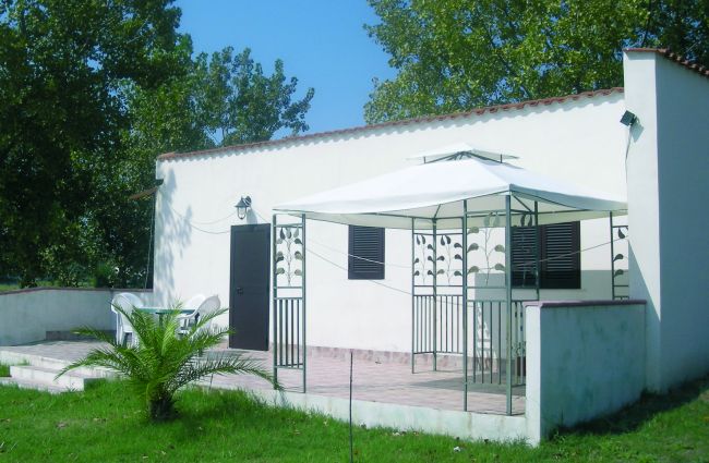 Piccola casa bianca con gazebo su prato verde.