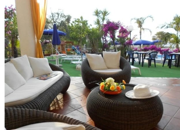 Area salotto con poltrone in vimini e vista giardino.