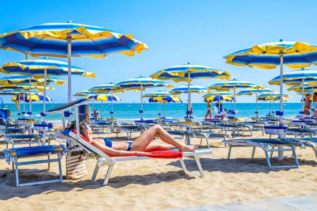 Donna su lettino sotto ombrelloni gialli e blu.