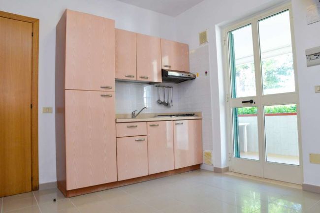 Angolo cottura con mobili in legno e porta finestra.