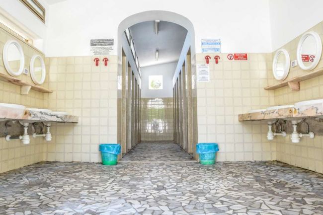 Bagno pubblico con specchi e lavandini su pareti opposte.